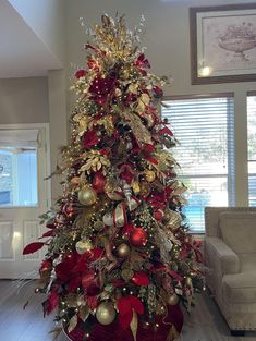 a christmas tree decorated with red and gold ornaments in a living room area next to a couch