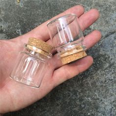 two small glass jars with corks are held in someone's hand