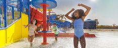 three children playing in the water at a splash park, one girl wearing a blue swimsuit