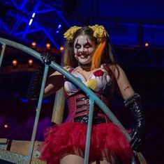 a woman dressed up as a clown on stage with her hands in the air while holding onto a railing