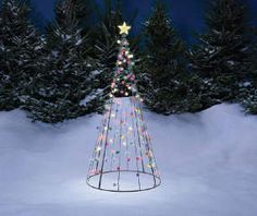 a lighted christmas tree in the middle of snow covered ground with evergreen trees behind it