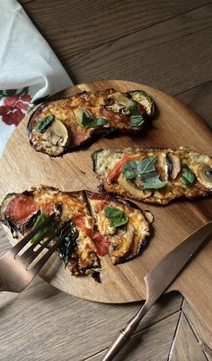 a wooden plate topped with slices of pizza next to a knife and fork