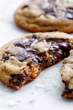 two chocolate chip cookies with one broken in half and the other partially eaten, on a white surface