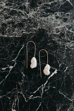 two white pearls are hanging from gold earwires on a black marble countertop