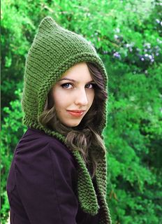 a young woman wearing a green knitted hat and scarf in front of some trees