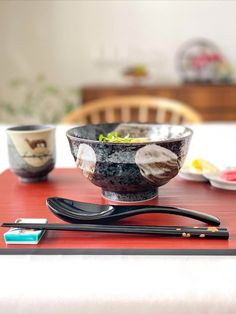 a bowl with chopsticks sitting on top of it next to a plate and fork