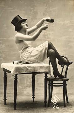 a woman sitting on top of a chair holding a glass in her right hand and wearing a hat