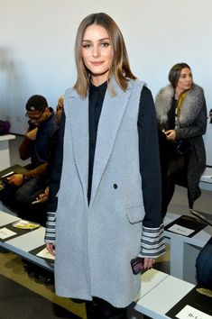 a woman standing in front of a group of people at a fashion show wearing black and grey