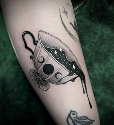 a black and white image of a teacup tattoo on the right arm, with a bird flying by it