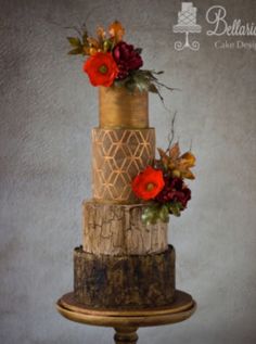 a three tiered cake decorated with red flowers and greenery on a wooden stand