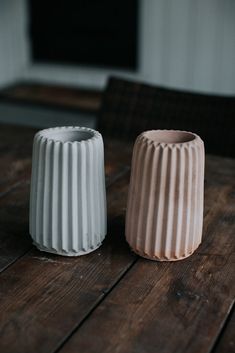 two white vases sitting on top of a wooden table next to eachother