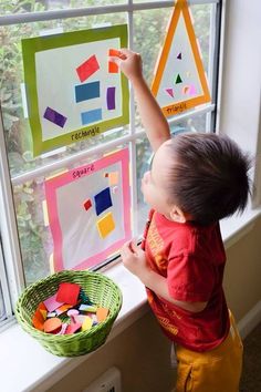 a little boy that is standing in front of a window with some papers on it