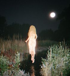 a naked woman is walking in the water at night with her back turned to the camera