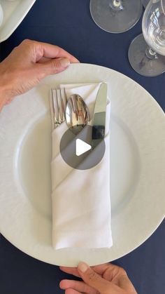 two hands holding silverware on top of a white plate with napkins and wine glasses