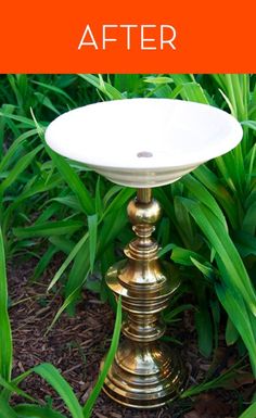 a gold pedestal with a white bowl on it in front of green plants and grass