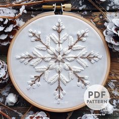 an embroidered snowflake is shown in the hoop with pine cones and branches around it