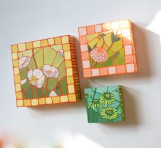 three square tiles with flowers painted on them sitting next to each other in front of a white wall