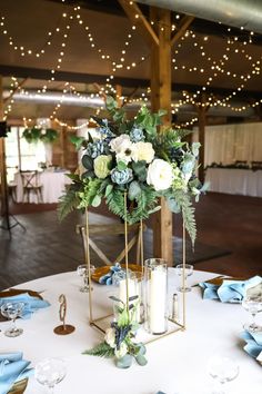 a centerpiece with candles, flowers and greenery sits on a white table cloth