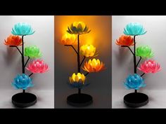 three different colored flowers on a black stand with a yellow light behind them and the same color