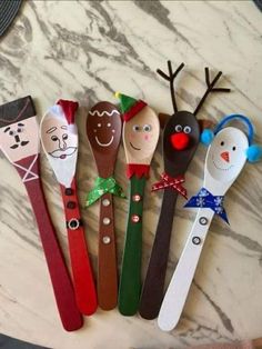 five wooden spoons decorated with christmas faces and reindeer noses, on a marble surface