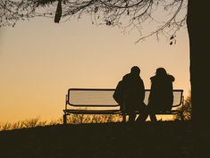 two people sitting on a park bench at sunset