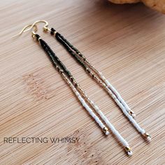 two long white and black beaded earrings sitting on top of a wooden table next to a pumpkin