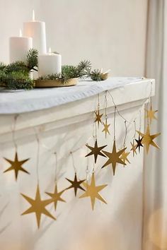 a mantle decorated with candles and evergreen branches, surrounded by gold stars hanging from the mantel