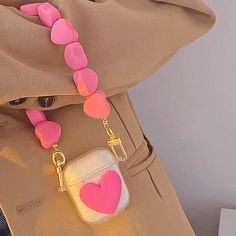 a pink and white heart shaped bag charm attached to a tan jacket with a gold chain