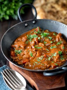 a pan filled with meat and vegetables on top of a wooden cutting board next to a fork