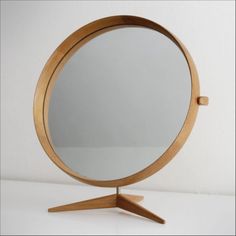 a round mirror sitting on top of a wooden stand in front of a white wall