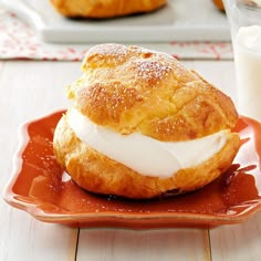 a pastry with cream on it sitting on a red plate next to a glass of milk