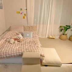 a small white dog laying on top of a bed next to a laptop and ottoman