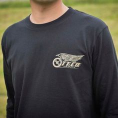 a man wearing a black long sleeved shirt with an old style motorcycle logo on it