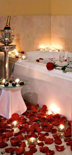 a bathtub with candles and rose petals on the floor next to it, surrounded by roses