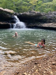 two children are playing in the water near a waterfall and some rocks, while another child is swimming