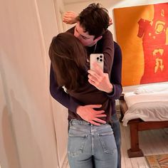 a man and woman hug in front of a mirror while taking a selfie with their cell phone