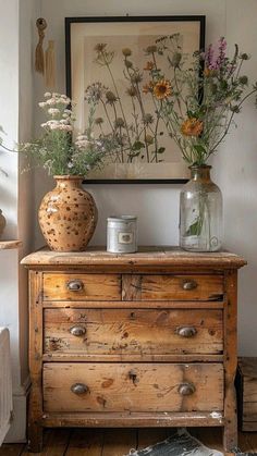 an old dresser with flowers in vases on top and a painting hanging above it