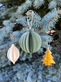 three paper ornaments hanging from a pine tree