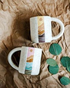 two coffee mugs sitting next to each other on top of a piece of paper