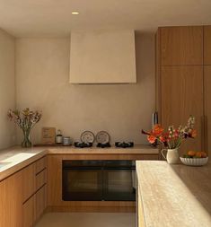 a kitchen with wooden cabinets and white counter tops, an oven in the corner and flowers on the counter