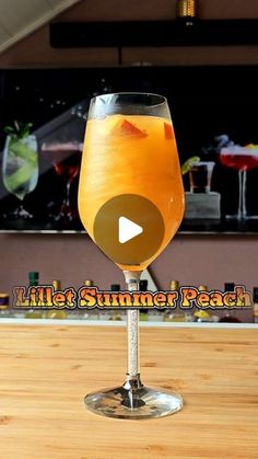 a glass filled with orange liquid sitting on top of a wooden table next to a bar