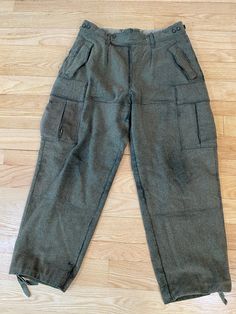 These thick warm wool vintage German military pants  are so well made that, though they are showing some wear, they have lots of life left in them. There is thick stitching everywhere, buttons (with lined flaps!)  to secure all the pockets, and ties at the bottom of each leg to tighten it or button it up shorter as needed. They are high-waisted with a button fly and a double button front closure (one of the buttons is missing). Each side of the waistband has a button adjustment to tighten the wa Vintage Winter Bottoms With Pockets, Retro Winter Trousers, Vintage Cargo Pants With Pockets For Fall, Vintage Fall Cargo Pants With Pockets, Vintage Trousers For Winter, Vintage Wide Leg Pants For Winter, Vintage Winter Trousers, Vintage Full Length Bottoms For Winter, Vintage Full-length Winter Pants