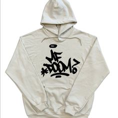 This Is The Mf Doom Hoodie With Mf Doom Graffiti On The Front And Big Madvilliany Mask On The Back On A Sand Colored Hoodie With Black Designs. White Cotton Hoodie With Graffiti Print, Urban Cotton Hoodie With Graffiti Print, Cream Hoodie Sweatshirt For Streetwear, Cream Drawstring Hood Sweatshirt For Streetwear, Cream Sweatshirt With Drawstring Hood For Streetwear, Cream Logo Print Top For Streetwear, Cream Hooded Hoodie For Streetwear, Cream Relaxed Fit Hoodie For Streetwear, Cream Tops For Winter Streetwear