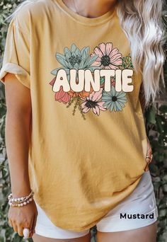 Auntie Shirt, Comfort Colors®, Floral Auntie TShirt, Flower Graphic Tee, New Aunt Gift, Pregnancy Announcement, New Baby Gift for Sister SIZE UP for an OVERSIZED FIT (see size chart in listing photos). Our shop uses direct-to-garment printing to make our products. The design ink is sprayed on, then allowed to soak into the fibers of the garment. This process yields fine quality prints and a smooth finish on the garment. COMFORT COLORS Garment-dyed t-shirt, made 100% with ring-spun cotton. The soft-washed, garment-dyed fabric brings extra coziness to your wardrobe while the relaxed fit makes it an excellent daily choice. The double-needle stitching throughout the tee makes it highly durable while the lack of side-seams helps the shirt retain its tubular shape. Relaxed Fit CARE Machine Wash Yellow Short Sleeve T-shirt For Family Matching, Casual Yellow Tops With Name Print, Spring Family Matching Crew Neck T-shirt, Family Matching Letter Print T-shirt For Spring, Yellow Cotton Tops With Name Print, Yellow Short Sleeve T-shirt With Name Print, Yellow Short Sleeve Top With Name Print, Cute Relaxed Fit Tops With Name Print, Casual Family T-shirt For Spring