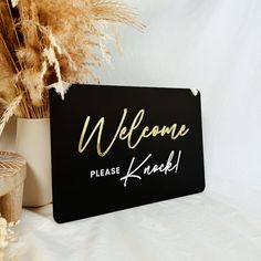 a welcome sign sitting on top of a table next to some dried plants and a potted plant