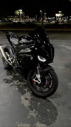 a shiny black motorcycle parked in a parking lot at night with its lights turned on