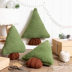 three knitted christmas trees sitting on top of a wooden floor next to yarn balls