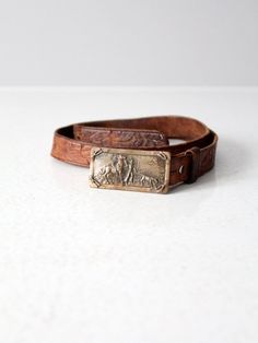 This is a vintage tooled leather belt with brass buckle.  The saddle brown leather belt has a classic western floral pattern.  A removable brass buckle pictures a cowboy with his horse and calf. CONDITIONIn good condition with wear consistent with age and use. MARKED SIZE:  30FITS: 29" - 32.5"MEASUREMENTSStrap Length:  34.5"  ..  87.6 cmStrap Width:  1"  .. 2.54 cmBuckle:  2.75" x 1.375"  ..  7 cm x 3.5 cm121941 Vintage Engraved Leather Belt, Vintage Adjustable Belts And Suspenders With Brass Buckle, Vintage Leather Belts For Ranch, Vintage Engraved Brown Belt Buckles, Vintage Brown Engraved Belt Buckles, Vintage Brown Hand-tooled Belt Buckle, Vintage Adjustable Belt With Brass Buckle, Vintage Brown Belts And Suspenders With Antique Buckle, Vintage Leather Belts For Western-themed Events