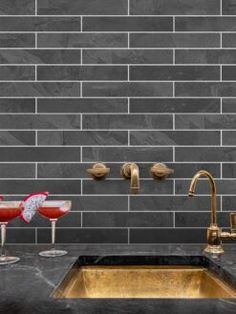 a kitchen with black marble counter tops and gold sink faucet, two glasses of red wine on the counter