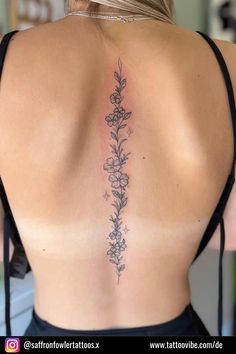 the back of a woman's neck with flowers and leaves tattooed on her lower back